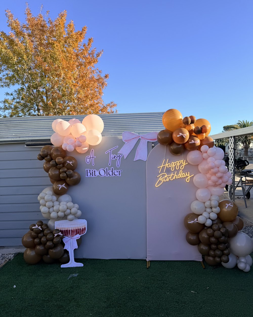 Two arched panels in cream and blush with brown, orange and cream balloon garlands and a neon sign